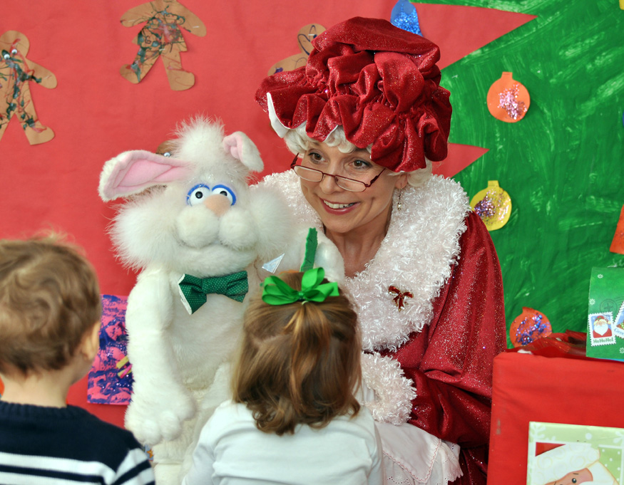Mrs. Santa entertains children with rabbit puppet.